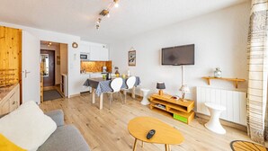 A compact living space with a sofa, a dining table with chairs, a TV mounted on the wall, and a small kitchen area. - Comfortable studio at the slopes for 4 people (Saint-François-Longchamp)