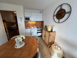 Cocina compacta con microondas, fregadero y estufa, una mesa de comedor con un jarrón de flores y un armario de madera con adornos.