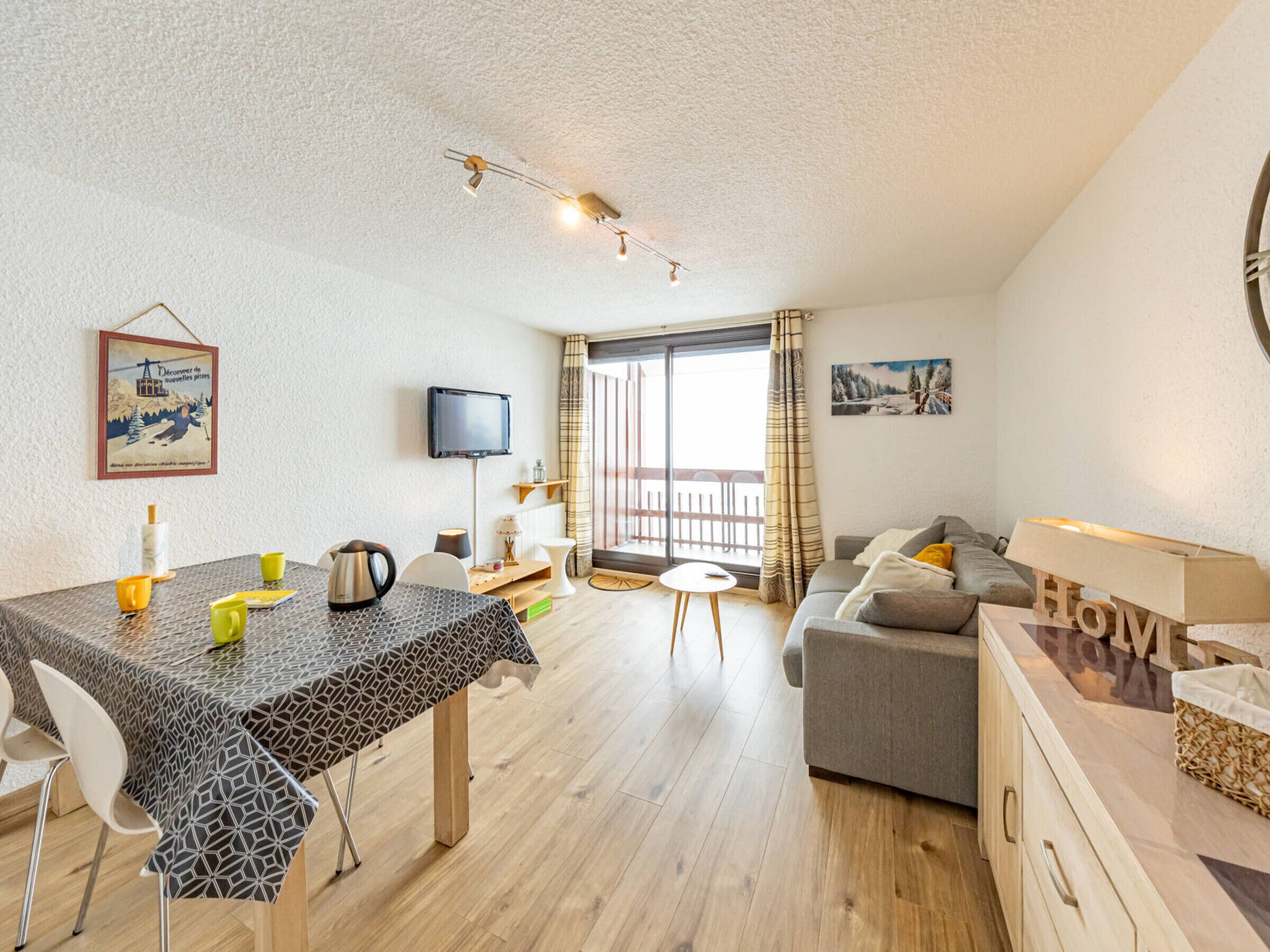 A modern, well-lit living area with a dining table, sofa, and TV.