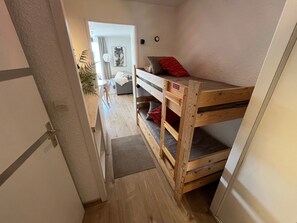 Una habitación con literas, una mesita y una puerta que da a otra estancia.