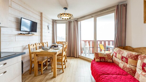Ein gemütlicher Wohnbereich mit einem Holzesstisch, Stühlen, einem roten Sofa und einem an der Wand befestigten Fernseher.