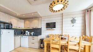 Eine moderne Küche mit Holzschränken, einem Esstisch mit Stühlen, einem an der Wand montierten Fernseher und einer Deckenleuchte.