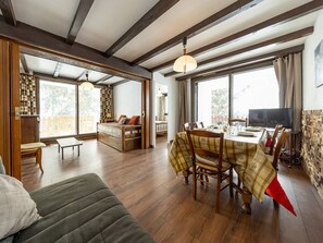 Ein geräumiges Zimmer mit Holzboden, einem Esstisch für vier Personen, einer Couch und einem Fernseher.