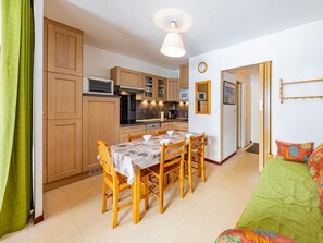 A compact kitchen with wooden cabinets, a dining table with four chairs, and a microwave.