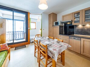 A modern kitchen with wooden cabinets, a dining table with chairs, and a large sliding glass door leading to a balcony.
