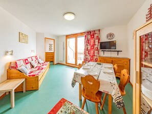Uma sala de estar acolhedora com um sofá, uma mesa de jantar posta para quatro pessoas e uma televisão.
