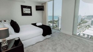 A modern bedroom with a large bed, a flat-screen TV, and a city view.