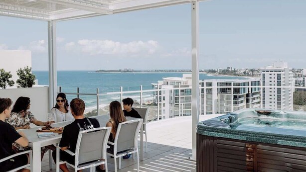 A terrace with a hot tub, dining area, and a view of the sea and buildings.