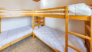 A room with three bunk beds, wooden ceiling, and white walls.