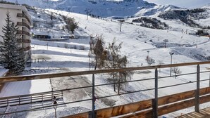 A snow-covered ski slope with a building on the left and mountains in the background.