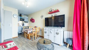 A compact living space with a dining area, kitchenette, and a TV mounted on the wall. - Modern 2-bedroom apartment at the foot of the slopes (Saint-François-Longchamp)