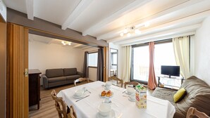 A dining area with a table set for breakfast, a sofa, and a TV in the background.