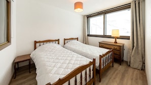 A bedroom with two wooden beds, a small bedside table, a lamp, and a window with curtains.