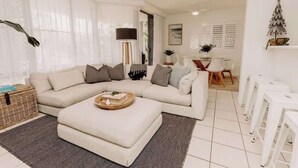 Una sala moderna con un sofá modular, una mesa de centro y un comedor con sillas blancas y una mesa.