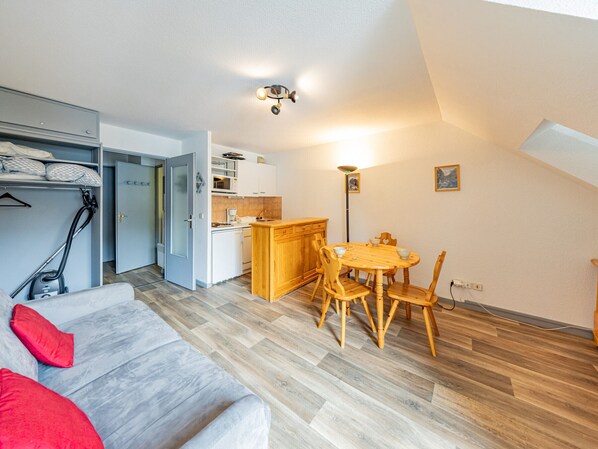 A compact living space with a kitchenette, dining area, and a sofa with red cushions.