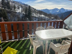 Een balkon met een glazen tafel en stoelen, met uitzicht op een besneeuwd berglandschap.