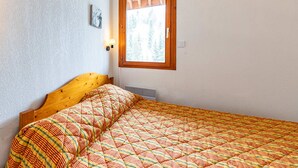 A bedroom with a wooden headboard, a quilted bedspread, a window with a view of trees, and a wall-mounted light fixture. - Comfortable apartment 7 ppl near slopes and shops (Saint-François-Longchamp)