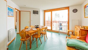 A room with a dining table, chairs, a sofa, a TV, and a window with a view of trees. - Comfortable apartment 7 ppl near slopes and shops (Saint-François-Longchamp)
