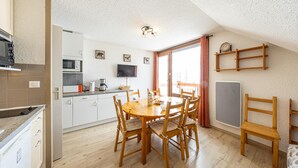 A compact kitchen with a dining area, a TV mounted on the wall, and a window with curtains.