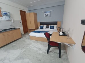 Habitación de hotel con cama, escritorio, silla, kitchenette y baño.