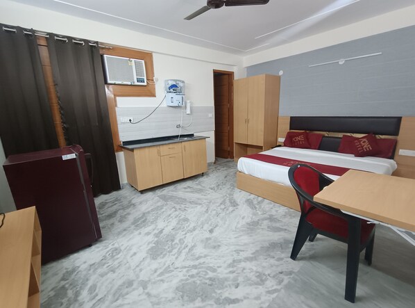 Habitación de hotel compacta con cama, escritorio, silla, kitchenette pequeña y refrigerador.