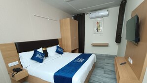 Ein Hotelzimmer mit Bett, Nachttisch, Kleiderschrank, Fernseher und einer kleinen Ablage.