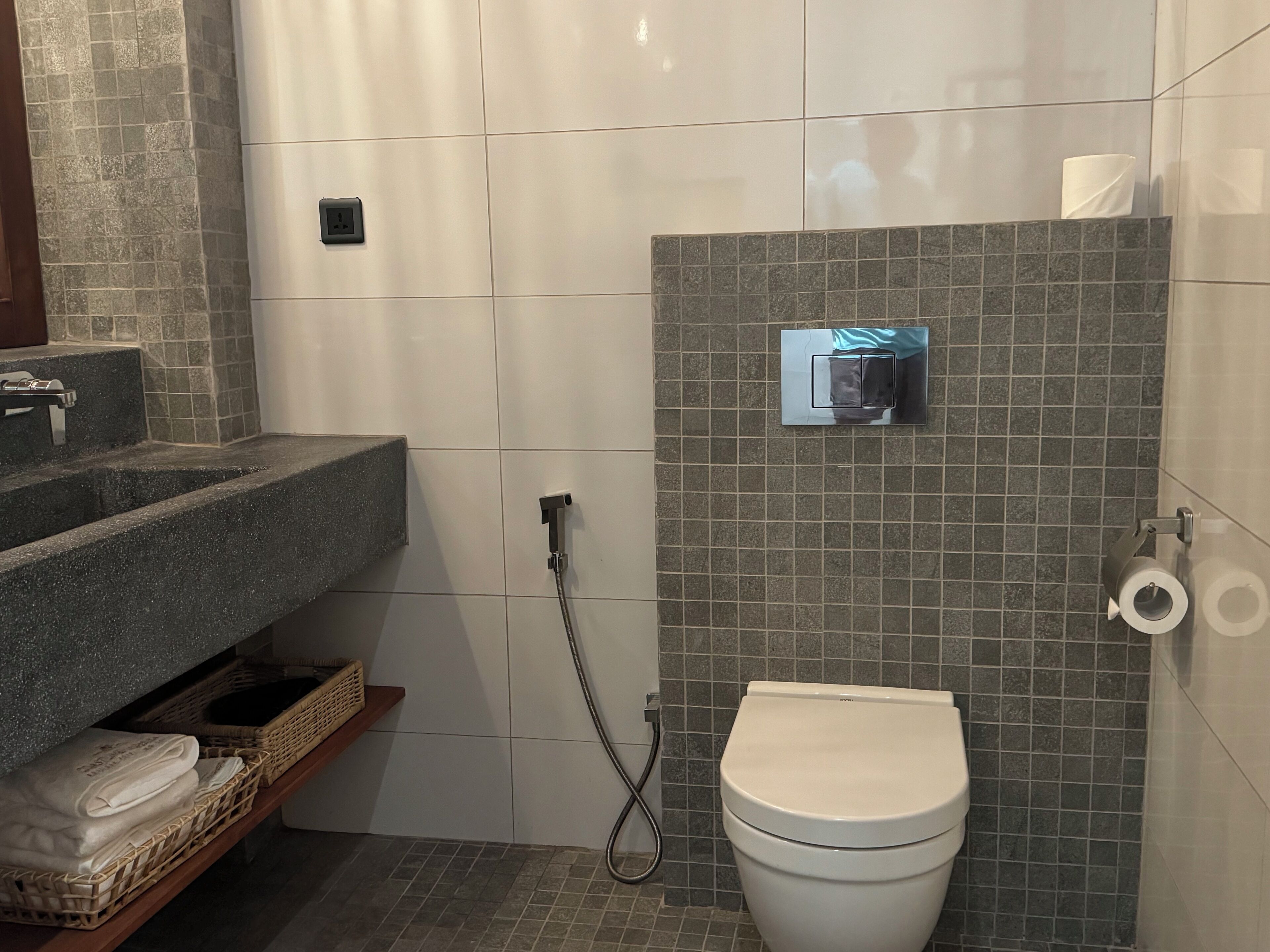 Un baño con inodoro blanco, ducha con cabezal de ducha manual, toallero y lavamanos con encimera.