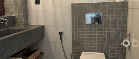 Un baño con inodoro blanco, ducha con cabezal de ducha manual, toallero y lavamanos con encimera.