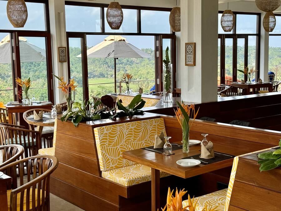 A restaurant with wooden furniture, large windows, and decorative plants.
