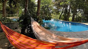 A hammock tied between trees near a swimming pool surrounded by lush greenery.