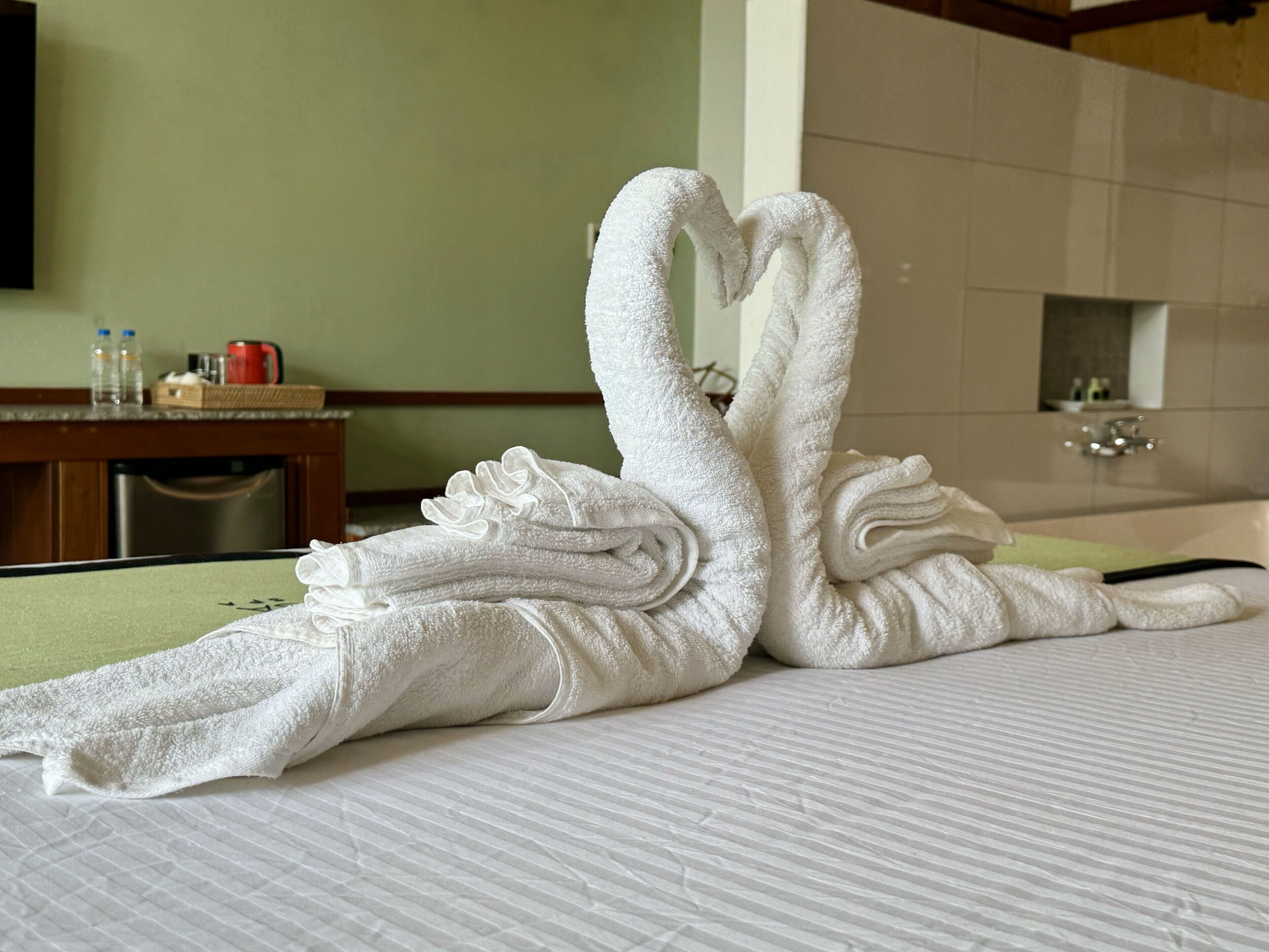 A neatly made bed with a towel arranged in the shape of two swans.