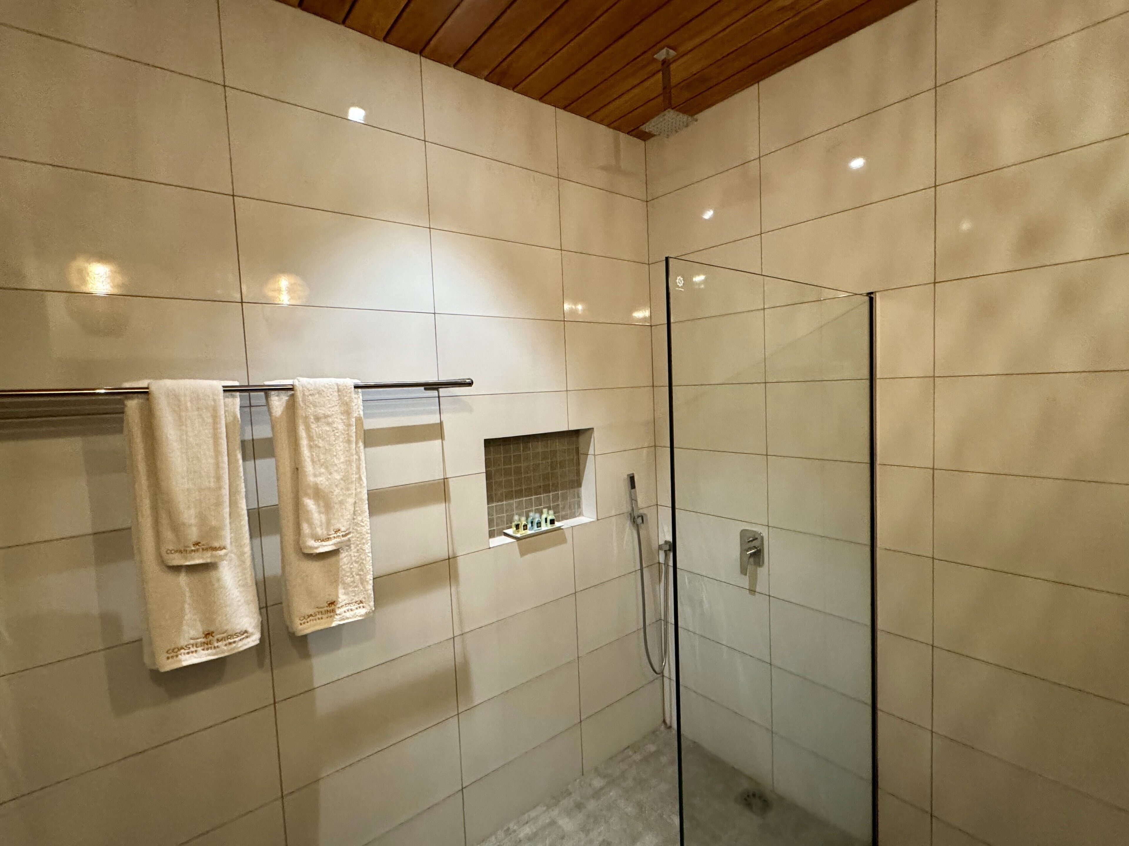 A modern bathroom with a glass shower enclosure, a towel rack with two towels, and a small shelf with toiletries.