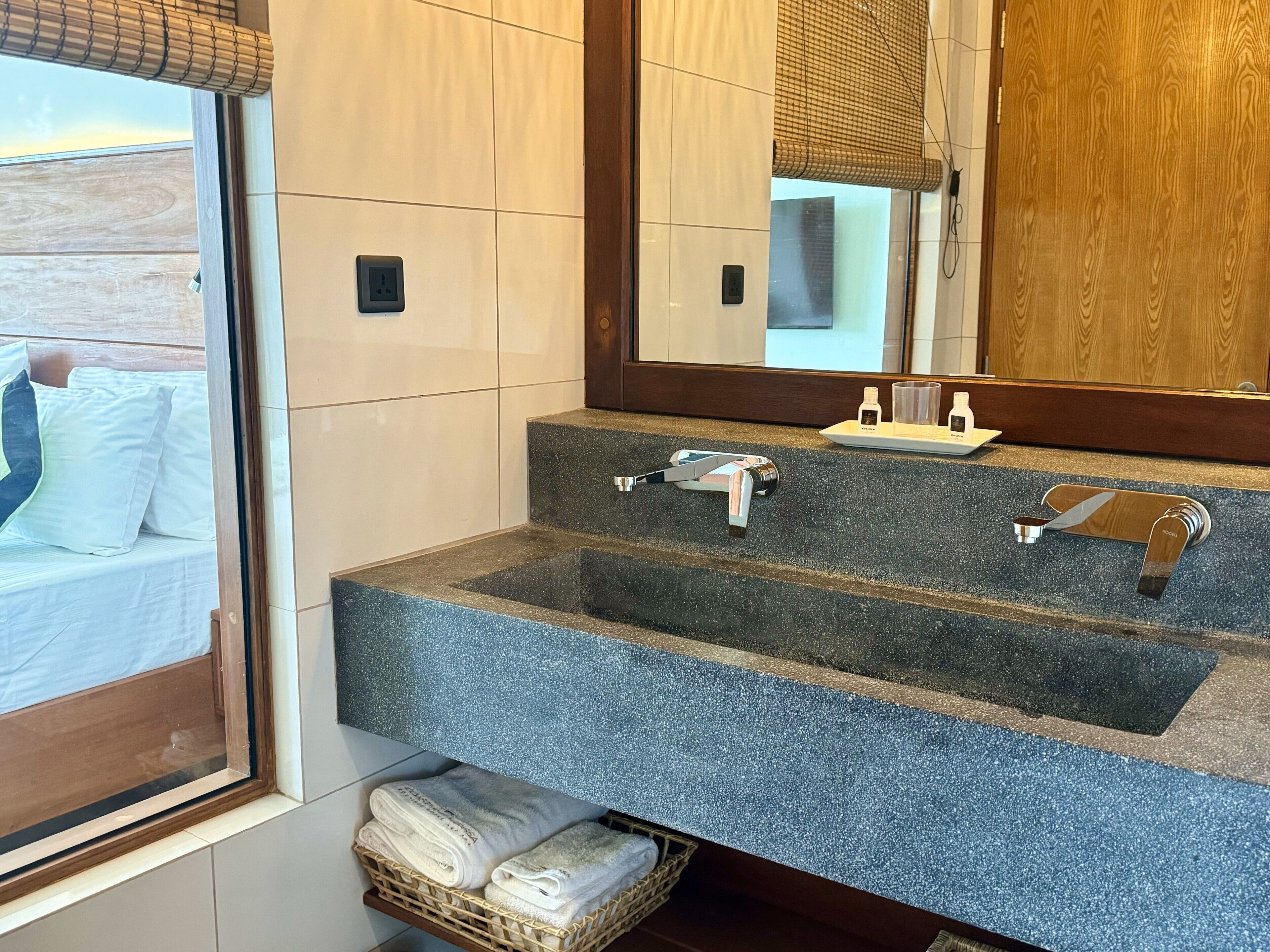 Un bagno con un lavabo in granito, uno specchio e una finestra con persiane.