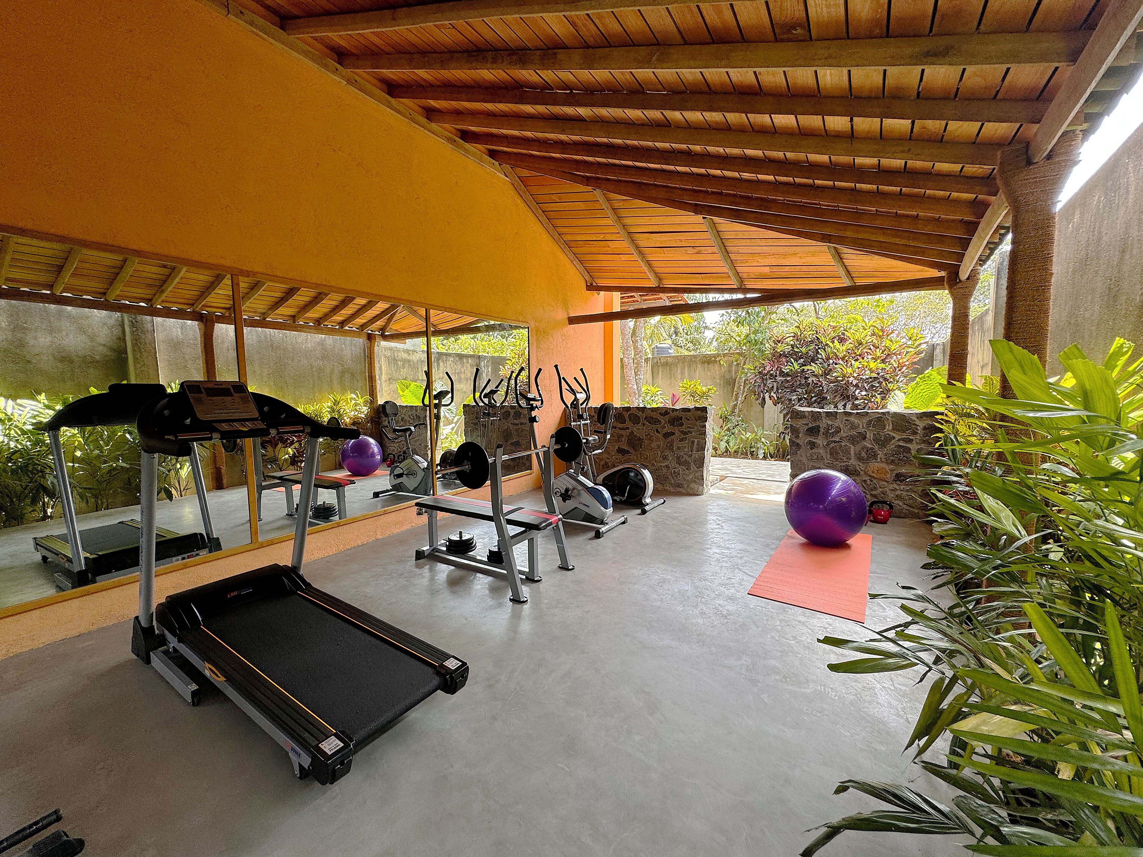 A covered outdoor gym area with exercise equipment, a treadmill, and exercise balls.