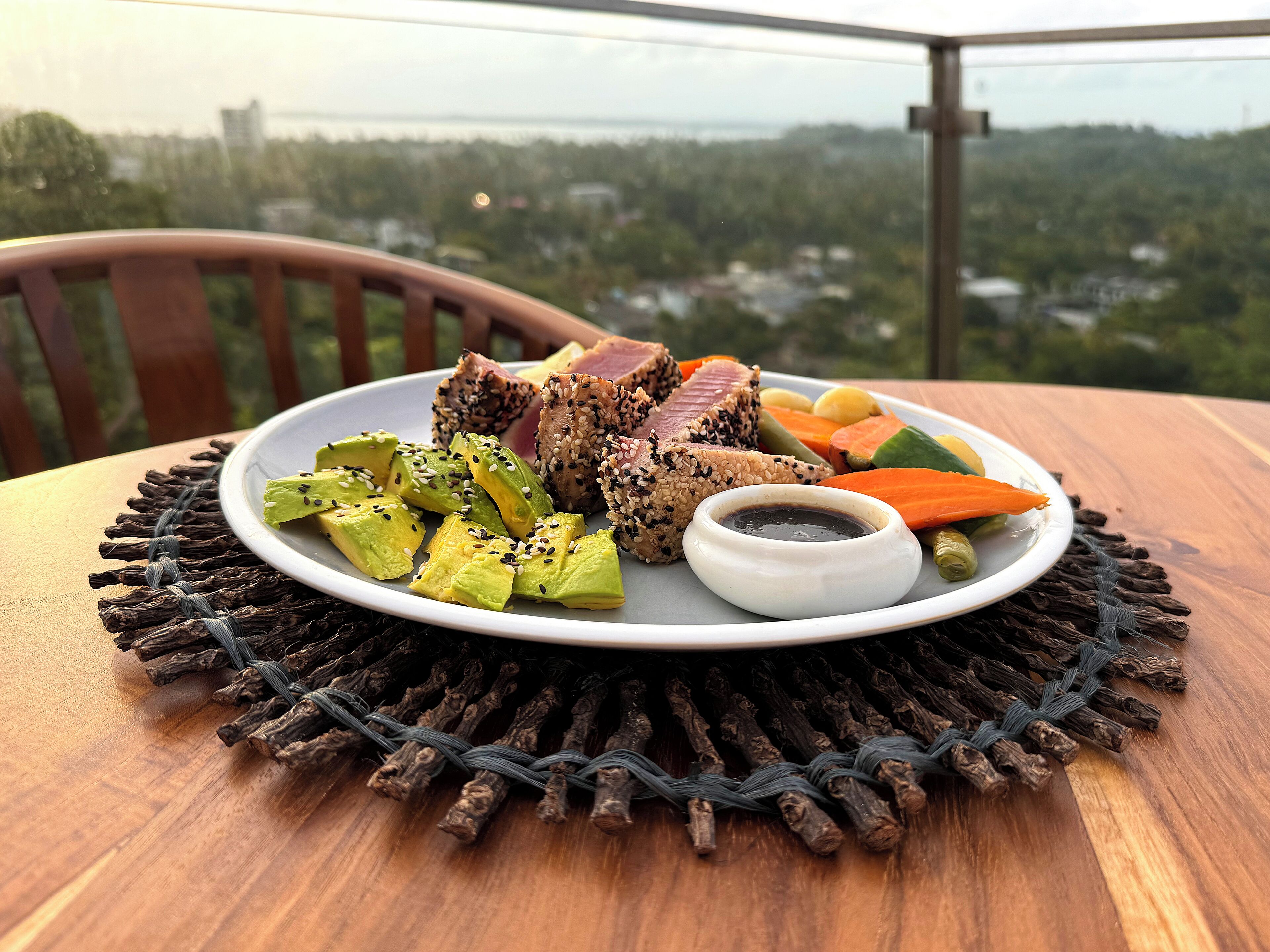 A plate of food with avocado, meat, and vegetables on a table with a view of a cityscape.