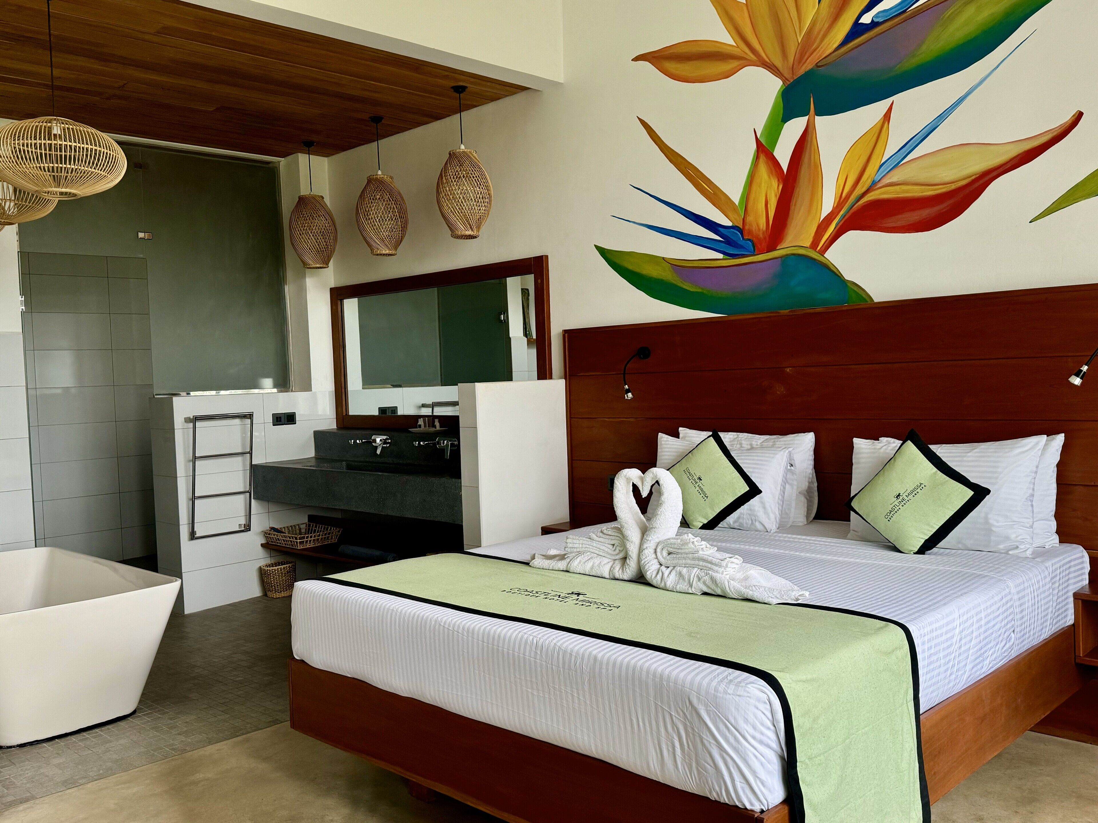 A hotel room with a wooden headboard, a large mirror, a bathroom with a white sink and vanity, and a colorful wall mural.