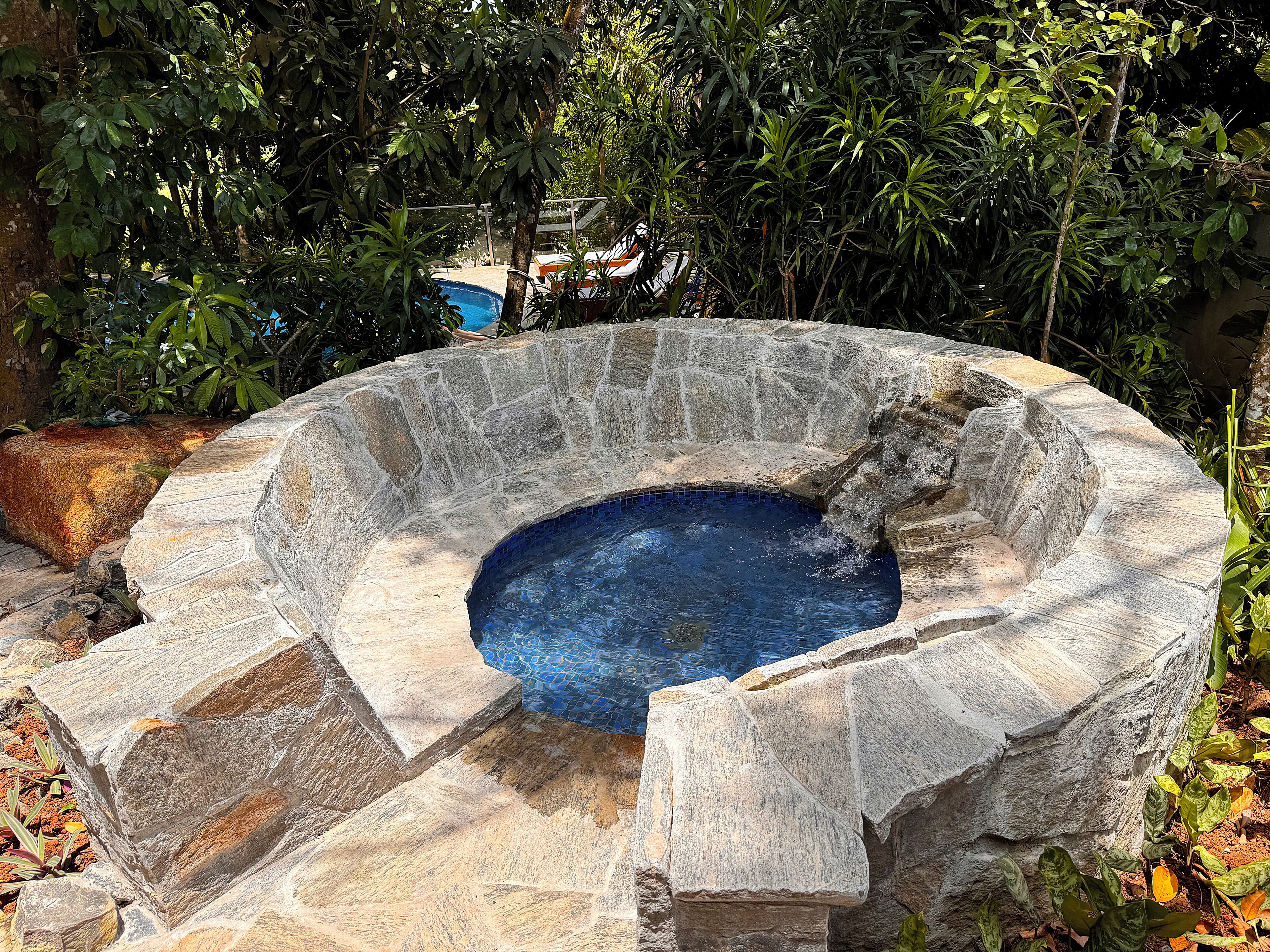 A stone hot tub surrounded by rocks and plants.