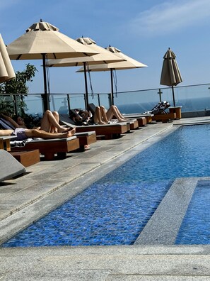 Un área junto a la piscina con sillones de descanso y sombrillas, una piscina con baldosas y una vista despejada del océano.