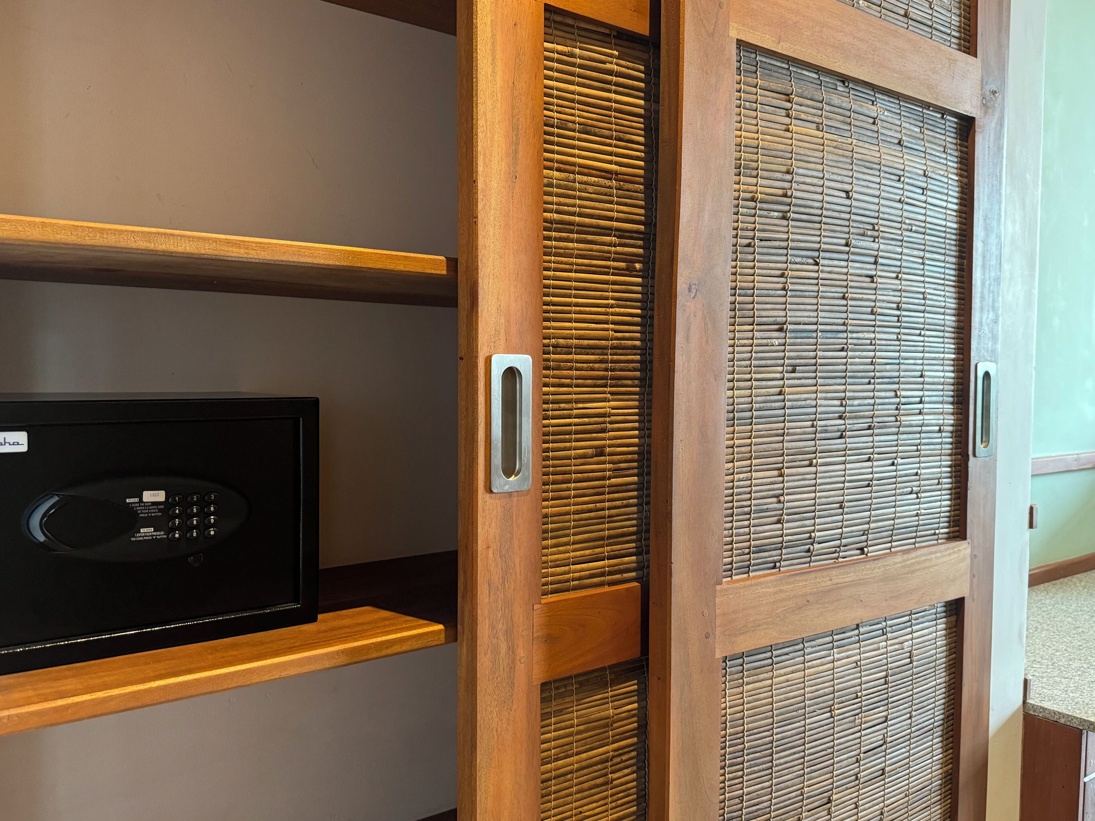 A room with a wooden door with a metal handle, a black electronic device on a wooden shelf, and a woven bamboo screen.