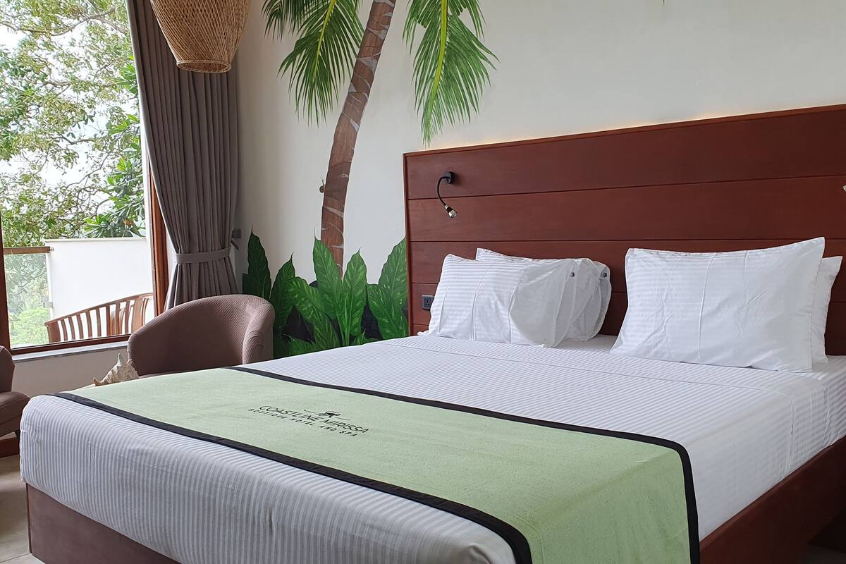 Una cama bien hecha con sábanas blancas y una manta verde, un cabecero de madera y vistas a la vegetación.