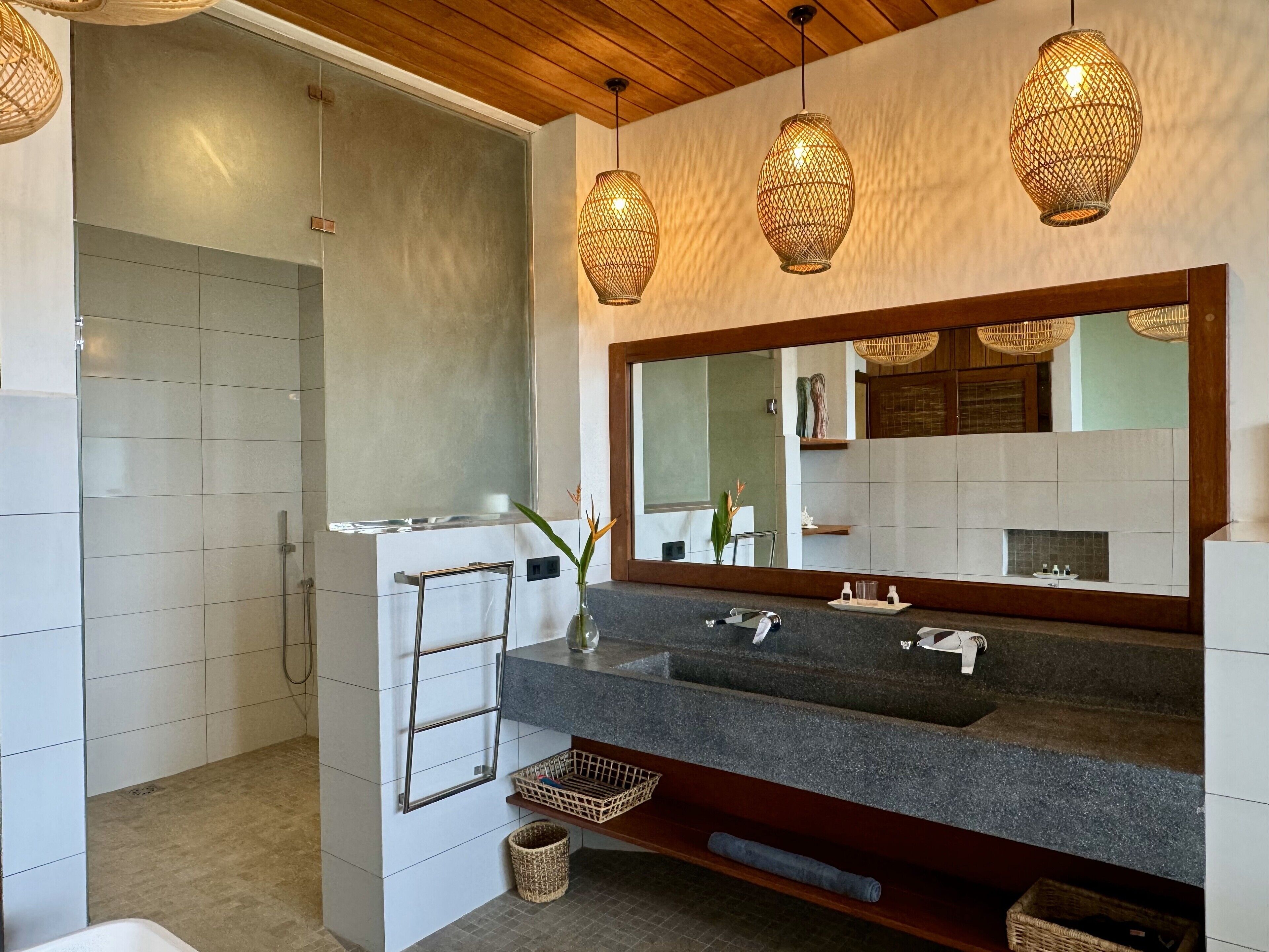 A modern bathroom with a large mirror, a vanity with a dark countertop, and a shower area.