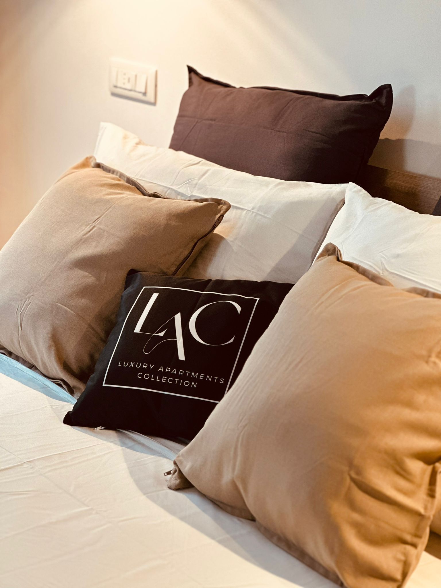 Ein Bett mit mehreren Kissen, darunter eines mit dem Schriftzug 'LAC Luxury Apartments Collection'.