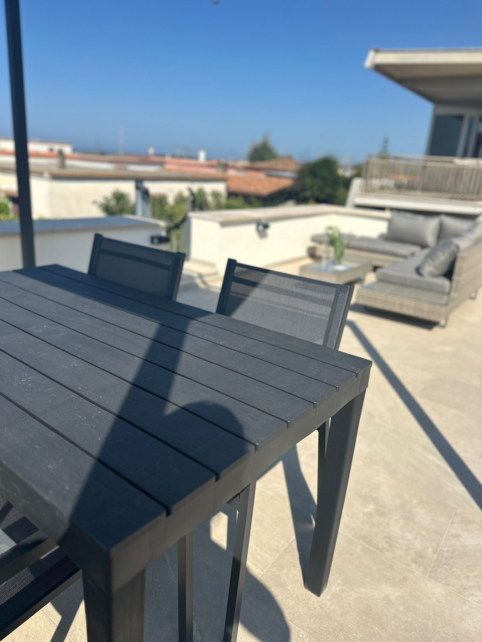 Eine Dachterrasse mit Tisch und Stühlen, einer Sitzecke und Blick auf entfernte Gebäude.