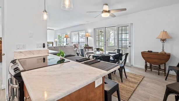 A modern kitchen with a large island, dining area with chairs, and a ceiling fan. - Bayfront Cottage -- Close to everything (St. Augustine)