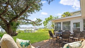 An outdoor patio with a dining table and chairs, a large tree, and a view of the ocean. - Bayfront Cottage -- Close to everything (St. Augustine)