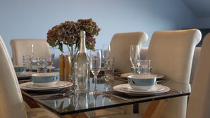 A dining table set with plates, bowls, glasses, and a vase with flowers. - The Chandlery - Panoramic Sea Views With Parking (Saundersfoot)