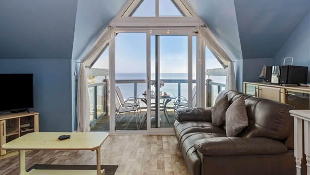 A modern living room with a large glass door leading to a balcony with a view of the sea. - The Chandlery - Panoramic Sea Views With Parking (Saundersfoot)