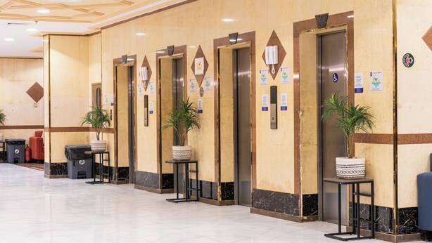 A hotel lobby with multiple elevators, potted plants, and a clean, tiled floor. - Safwat Almiead Hotel (Makkah)