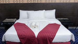 A neatly made bed with white linens, two rolled towels, and a red accent pillow. - Safwat Almiead Hotel (Makkah)