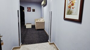 Un pasillo con suelo tipo espiga, una obra de arte floral enmarcada en la pared y un banco tapizado en color beige.